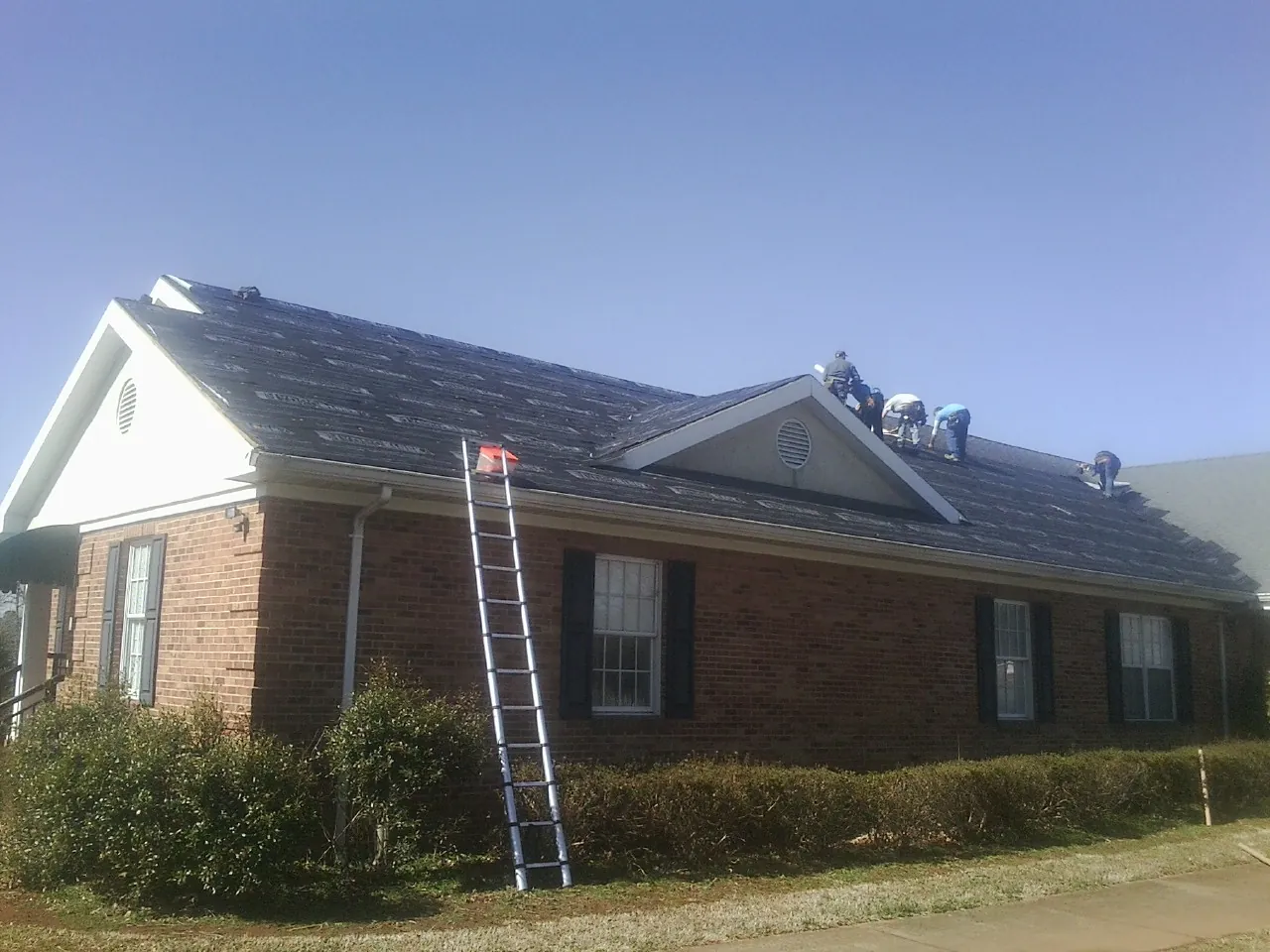 Crew tearing shingles off a brick ranch roof with a ladder set — Metal Roof Repair work by our crew in Peckville