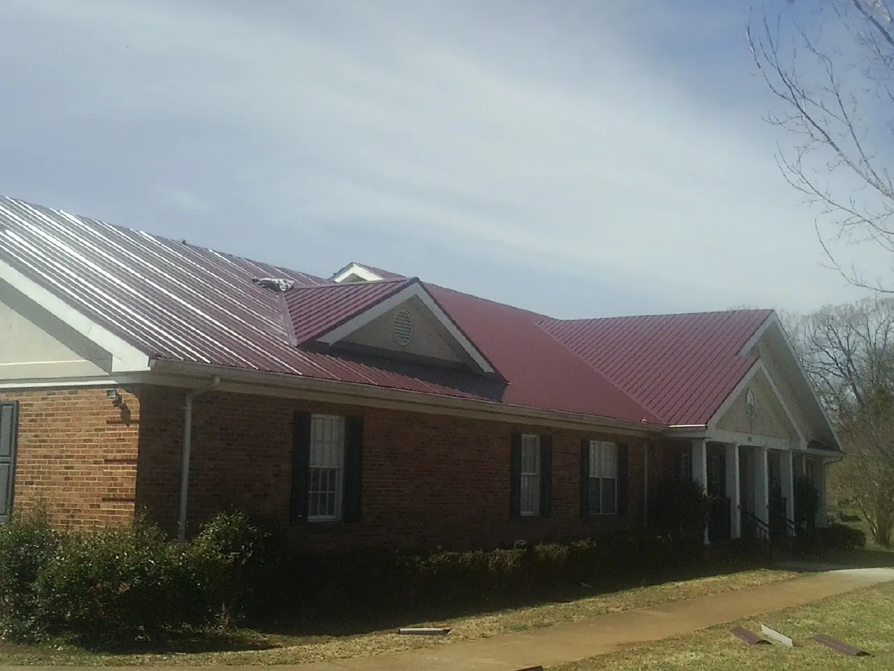 Red metal roof with gabled entries on a long brick building, from a Hail Damage Roof Repair job in Peckville