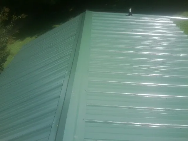 New green metal panels meeting at the ridge of a roof — Flat Roof Repair work by our crew in Peckville