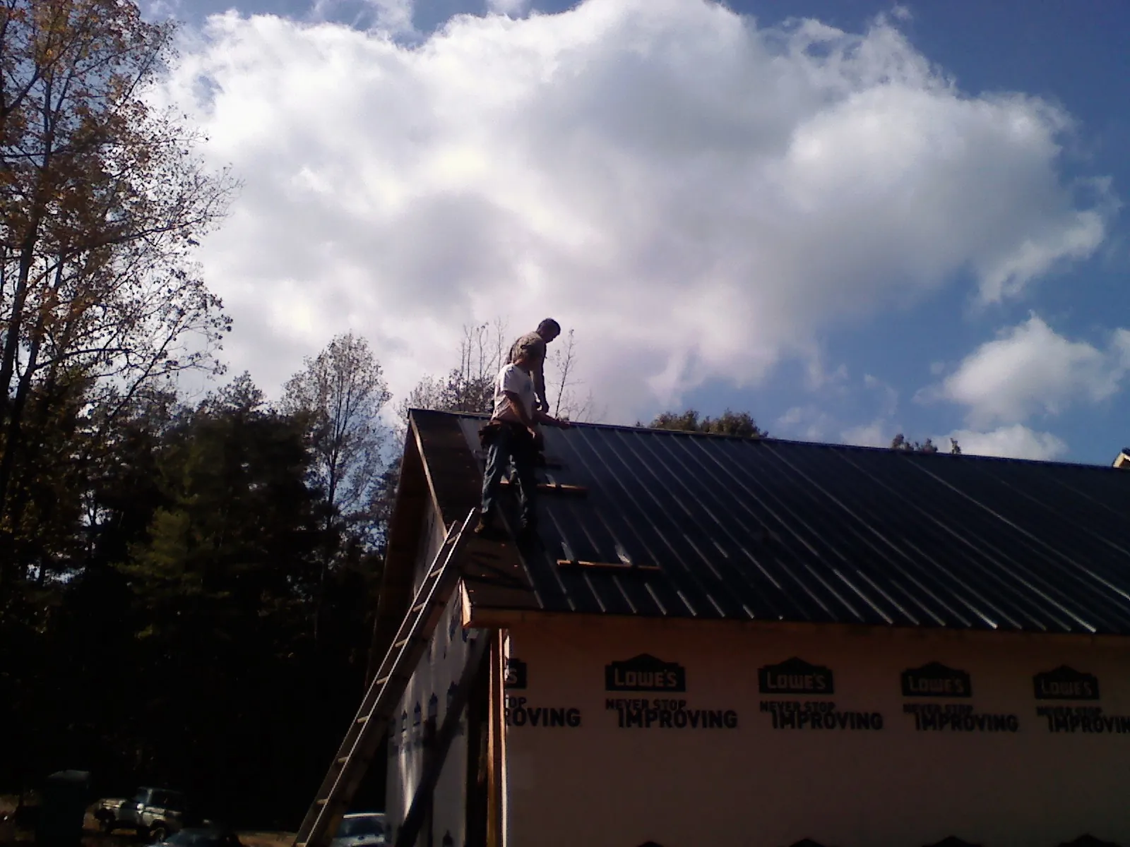 Roofer fastening dark metal panels high against a cloudy sky, from a Roof Inspection job in Peckville