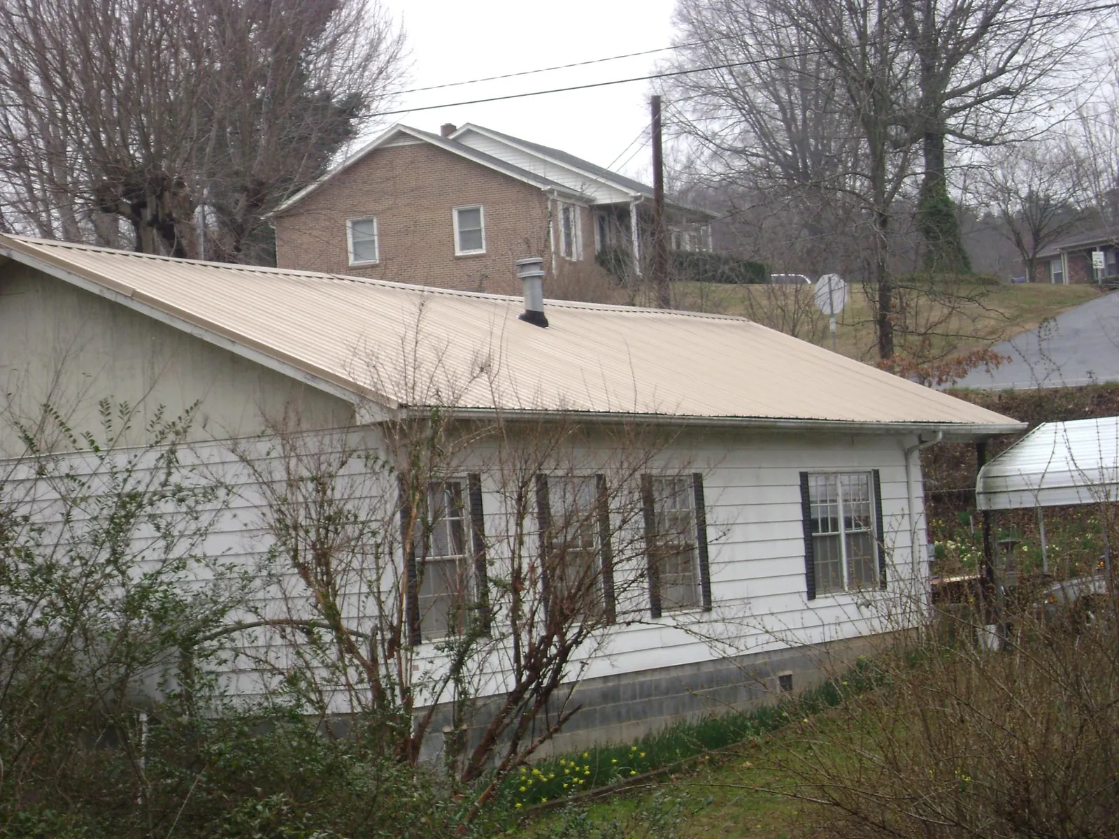 Tan metal roof on a white sided house set into a hillside — Commercial Roofing by Roofing Brothers in Peckville